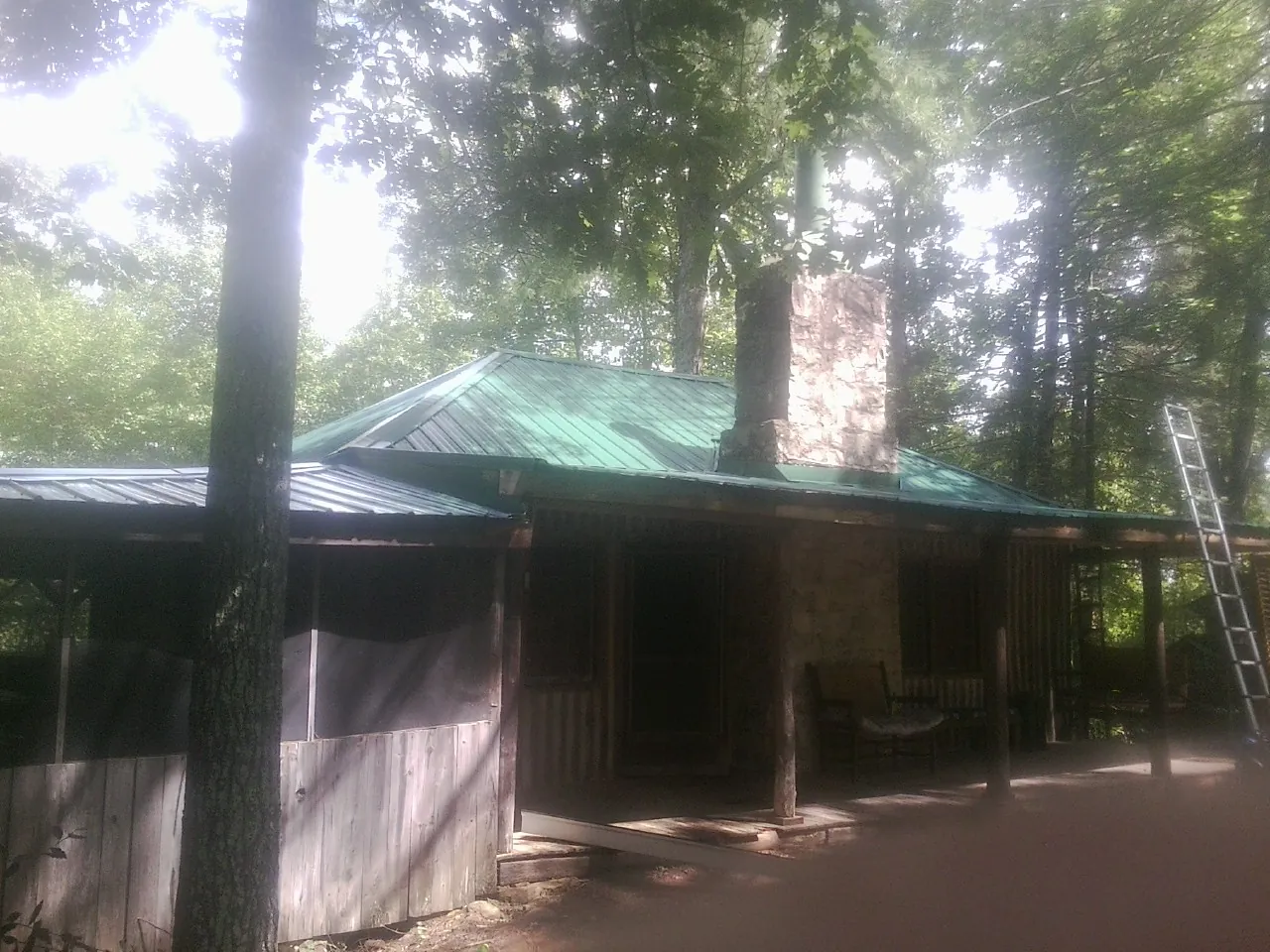 Green metal roof and stone chimney above a log cabin porch in Colchester