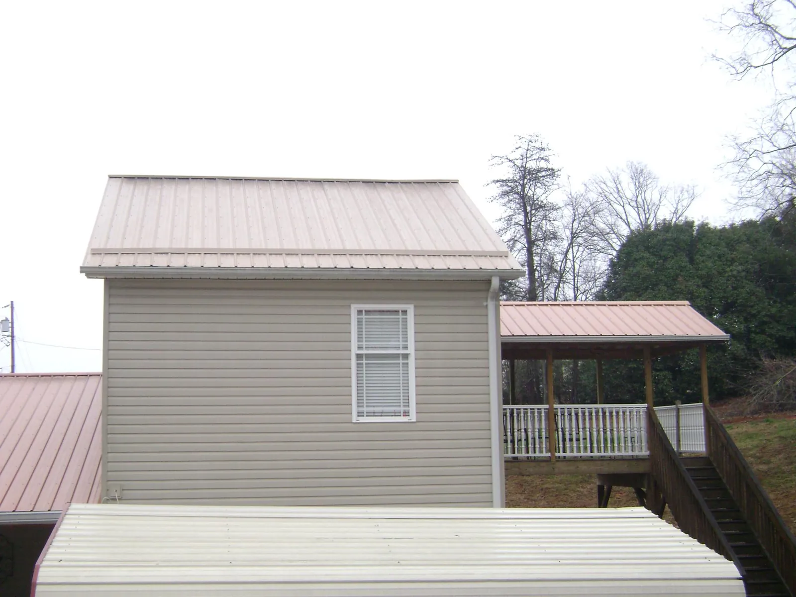 Tan metal roofs on a two story addition and attached porch, from a Roof Replacement job in Colchester